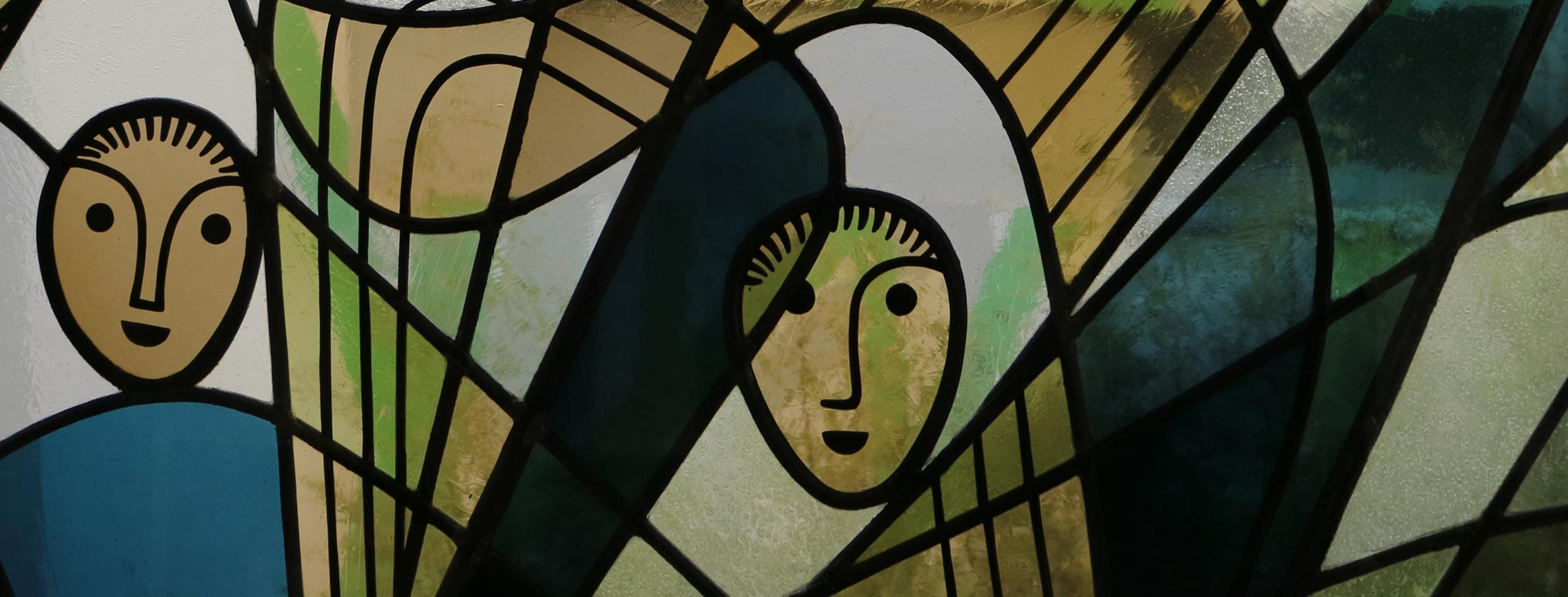 Detailaufnahme eines kunstvoll gestalteten Buntglasfensters mit abstrakten Engelsfiguren und harmonischen Grün- und Blautönen.